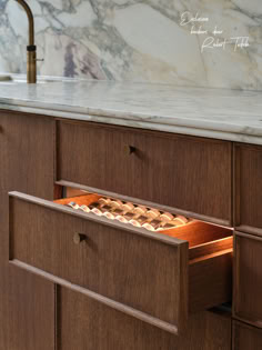 an open drawer in a wooden cabinet with marble counter top and white marble back splash