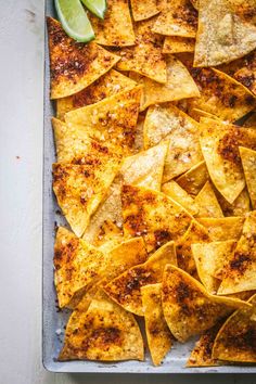 tortilla chips on a baking sheet with lime wedges next to the top