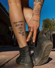 a person with tattoos on their legs and feet, holding onto a pair of shoes