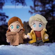 two dolls are standing in the snow holding hands with each other, one is wearing a yellow jacket and the other has blue eyes