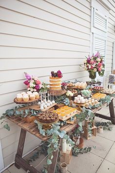 a table topped with cakes and cupcakes on top of wooden tables covered in greenery