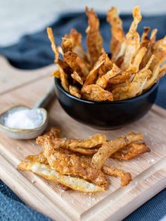 french fries in a black bowl on a cutting board next to a small container of salt and pepper