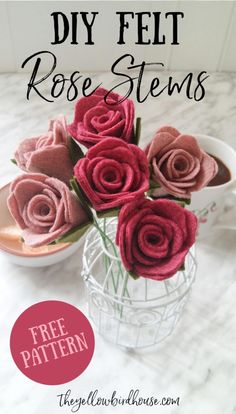 a vase filled with pink felt roses sitting on top of a table next to a cup