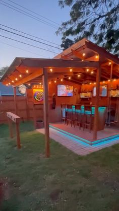 an outdoor bar is lit up at night with string lights on the roof and wooden posts