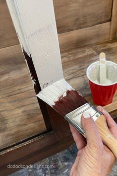 a person holding a paintbrush and painting the side of a wooden bench