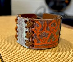 "One of a kind, upcycled leather bracelet made from used belts, upholstery scraps, and artistic findings. Every cuff is unique and made to wear and weather well.  Like high quality boots or your favorite leather journal, these cuffs get softer and more supple over time. The individual designs all start with the leather.  I use vintage belts, leather scraps, WW2 rifle holsters, and old horse bridles.  Each piece speaks to me, and informs the direction for the finished piece.  Adornments include found objects, printed leather, metal studs, gemstones, buttons - anything that will bring the cuff to life and make it a statement piece unlike any other. I prefer using a button & elastic closure when possible, as it makes the cuff fully adjustable.  It's a more labor and cost intensive process, bu Rustic Leather Bracelet For Festivals, Vintage Leather Bracelet With Patina, Rustic Handmade Leather Cuff Bracelet, Unique Handmade Leather Cuff Bracelet, Artisan Leather Bracelet With Patina, Artisan Leather Cuff Bracelet With Patina, Leather Cuff Bracelet With Patina Artisan Style, High Quality Boots, Horse Bridle