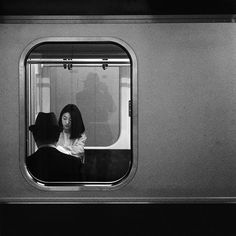 a woman sitting on a train looking out the window at another person standing next to her