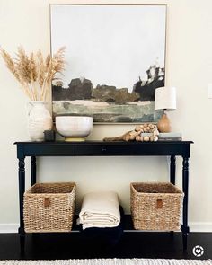 a black table with two baskets under it and a painting on the wall behind it