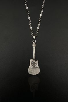 a guitar necklace is shown on a black surface with a silver ball chain around it