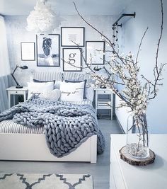 a bedroom with pictures on the wall and a bed covered in a blanket next to a vase filled with flowers