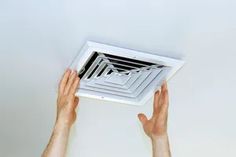 two hands are reaching up to the ceiling vent in front of a white wall,