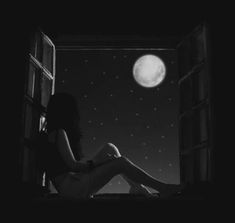 a woman sitting on the window sill looking out at the moon