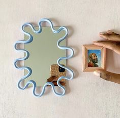 a hand holding a mirror next to a wall with a painting on it and a frame