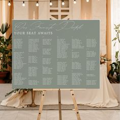 a seating chart on a wooden easel in front of a white table cloth draped with lights