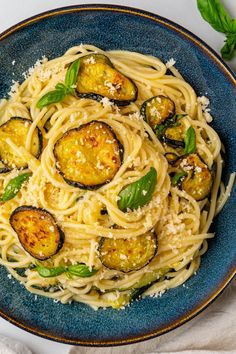 pasta with zucchini and parmesan cheese in a blue bowl on a white tablecloth