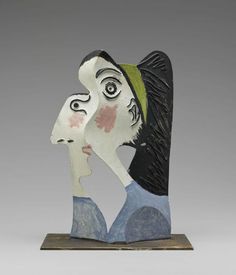 a ceramic sculpture of two people's faces on a wooden base with grey background