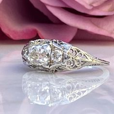 an antique diamond ring sits next to a pink rose