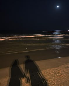 two people are standing on the beach at night with their shadows in front of them