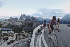 several people riding bikes on a road with mountains in the background and animals walking around