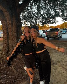 two women standing next to each other under a tree