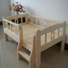 a wooden toddler bed sitting on top of a floor next to a vase with flowers