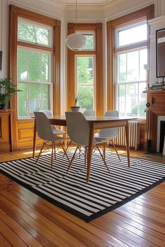 a dining room table with chairs and a rug in front of two windows that look out onto the woods