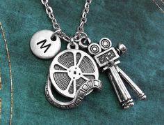 a silver necklace with two charms and a letter m on the front, sitting on a green velvet surface