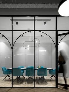 a glass walled meeting room with blue chairs and a round table in the foreground