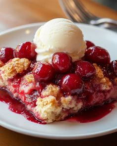 a piece of cherry cobbler with ice cream on top sits on a white plate