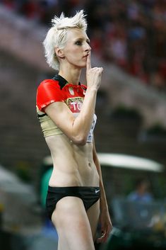 a woman with white hair wearing a red shirt and black shorts standing in front of a crowd