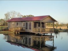 a small house sitting on top of a body of water next to a lush green field