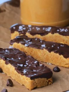 two pieces of chocolate covered cookie sitting on top of brown paper next to a cup