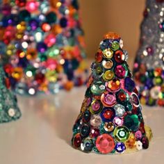 three small christmas trees made out of glass beads on a white counter top with other ornaments in the background