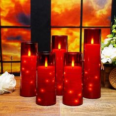 four red candles are sitting on a table next to a vase with flowers in it