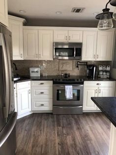 a kitchen with white cabinets and stainless steel appliances in the middle of wood flooring