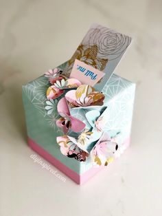 an open box with paper flowers on the inside, and a card attached to it