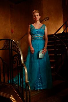 a woman in a blue dress standing next to some stairs