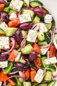 a salad with cucumbers, tomatoes, onions and feta cheese in a white bowl