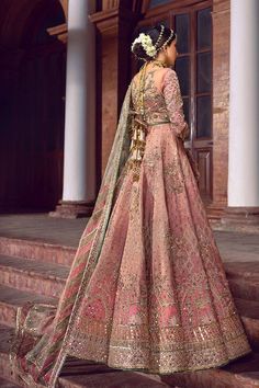 a woman in a pink lehenga standing on steps with her back to the camera