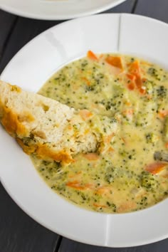 a white bowl filled with broccoli soup and a piece of bread on the side