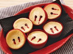 six cupcakes with faces drawn on them sitting in a red tray next to a fork and knife