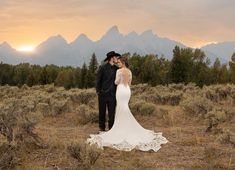 a bride and groom standing in the middle of a field with mountains in the background