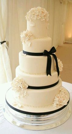 a white wedding cake with black ribbon and flowers