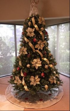 a christmas tree with gold bows and poinsettis on it in front of a window