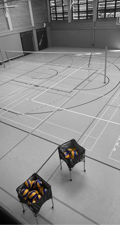 two chairs with yellow and blue balls in them on an indoor basketball court that is empty