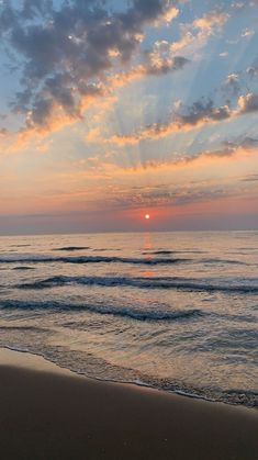 the sun is setting over the ocean with clouds in the sky and waves on the beach