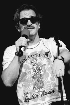 a man holding a microphone in his right hand and wearing sunglasses on top of him