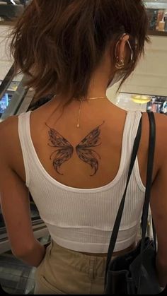 a woman with a butterfly tattoo on her back and shoulder, looking at an escalator