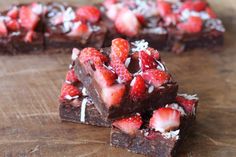 chocolate brownies topped with strawberries and coconut flakes on a wooden cutting board