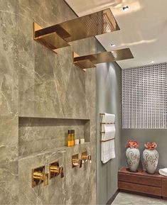 a modern bathroom with gold fixtures on the wall and marble tile flooring, along with two white vases